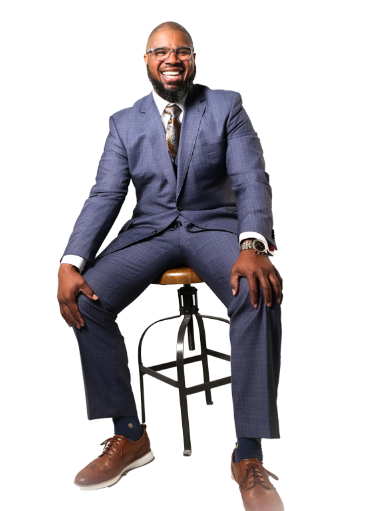 Man in a blue suit sitting on a stool, smiling confidently.